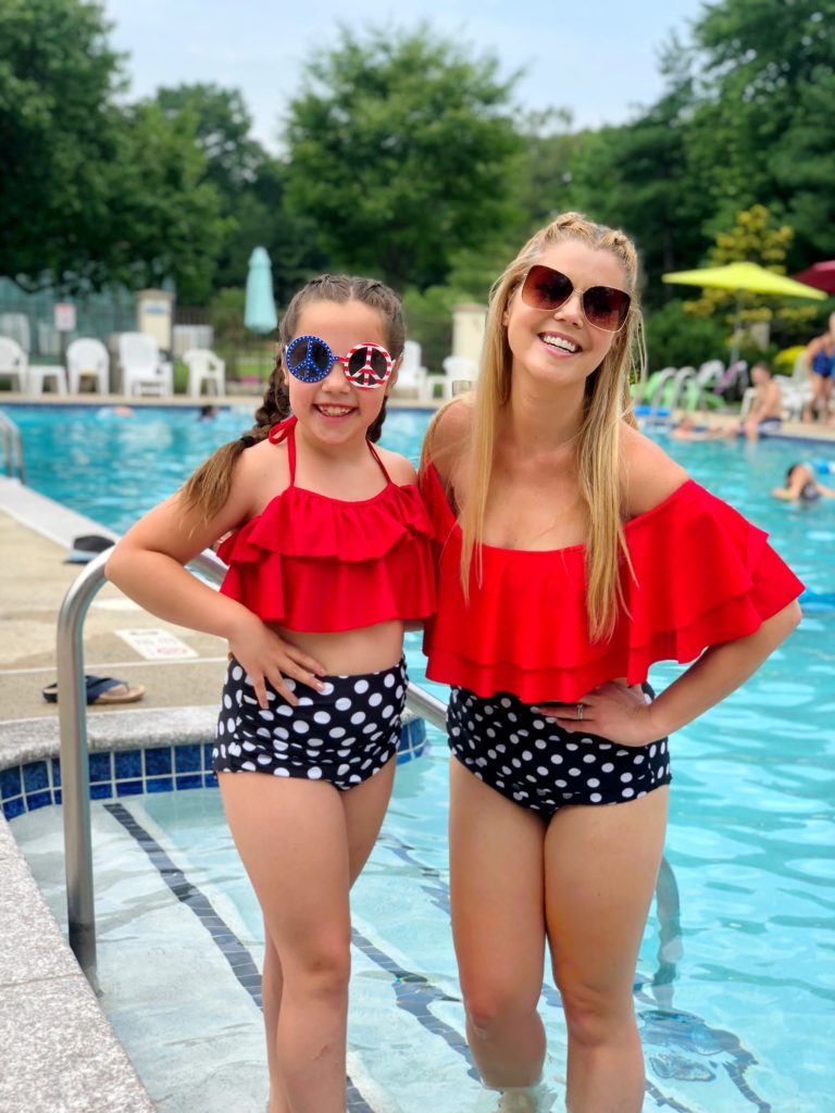A mother and daughter smile at the pool in matching swimsuits